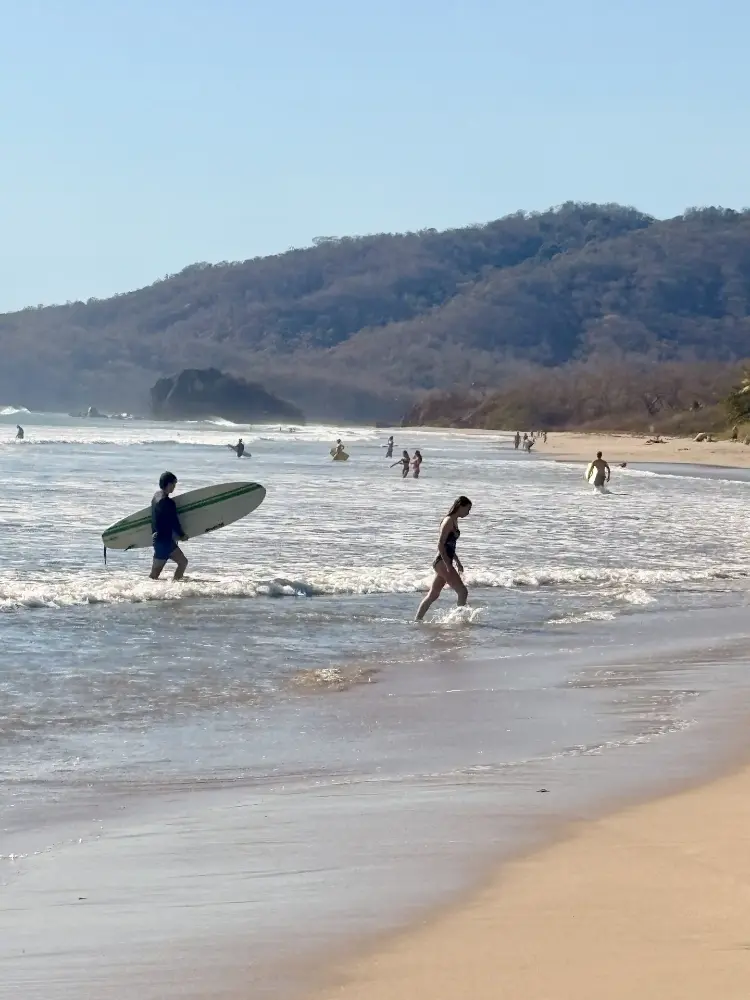 Surfer heading into the waves with a longboard at Playa Grande