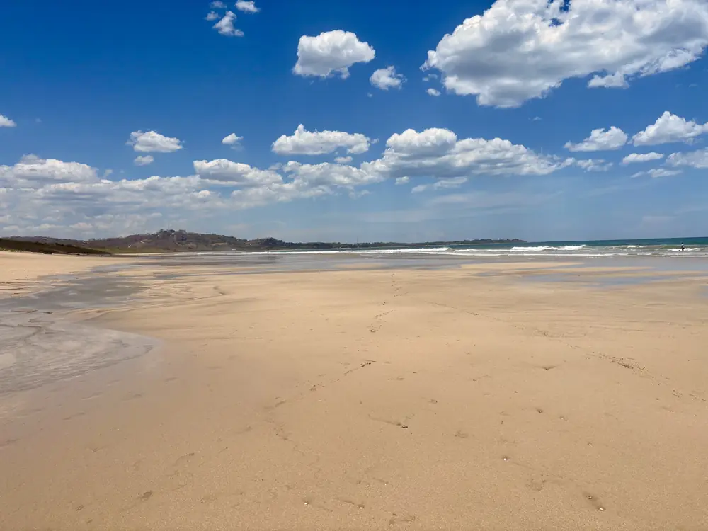 Wide, empty Playa Grande under a blue sky with puffy clouds